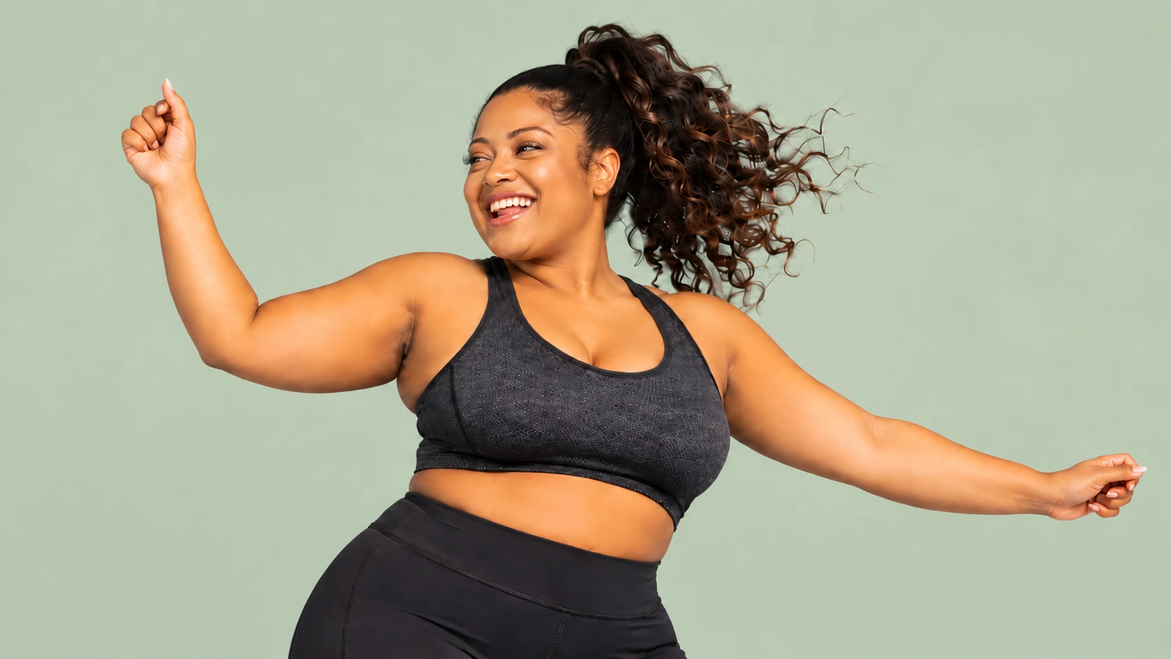 A smiling woman in activewear moving freely against a soft green background